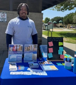 A man from the CWC street team stands outside at a booth for the Certified Wellness Coach profession at the Bulldog Lambada 5k run/walk.