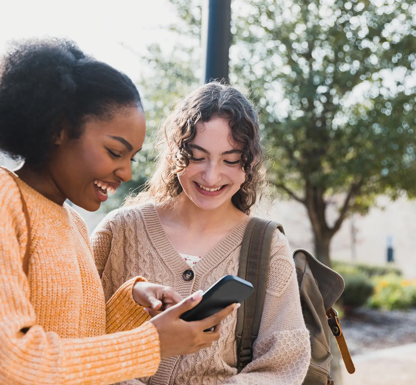 Two young teens look at a phone smiling.