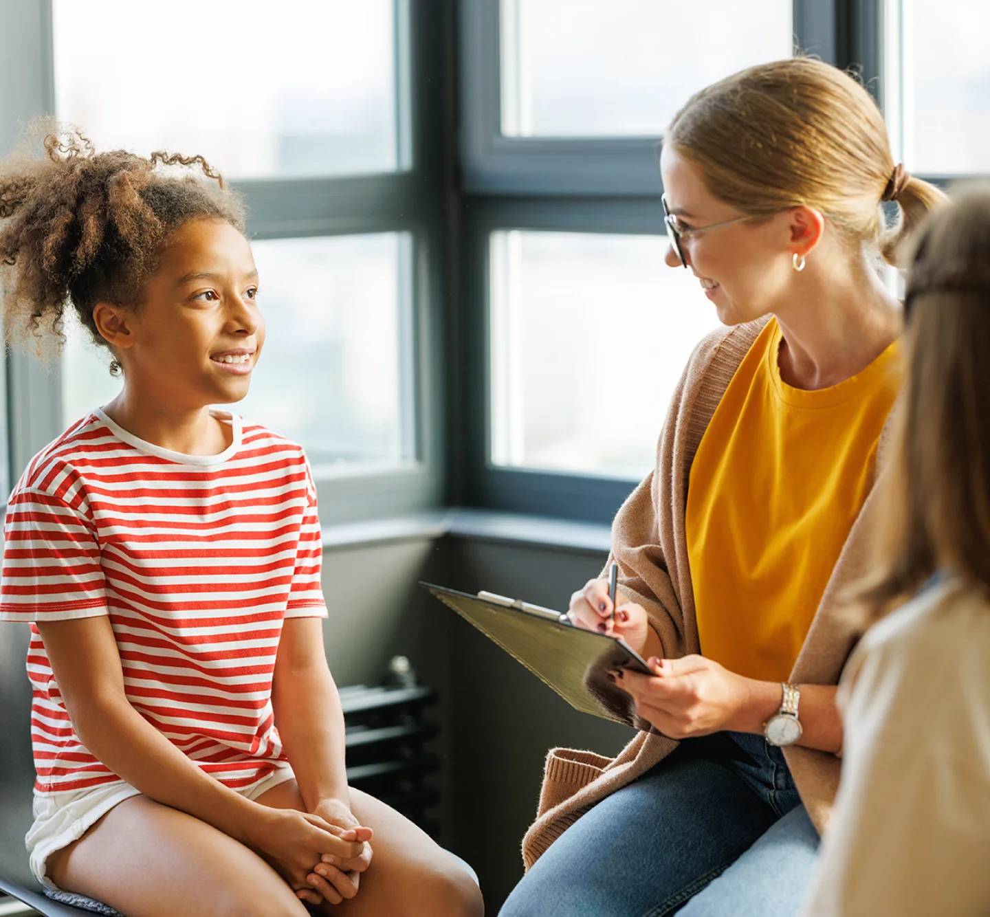 A Certified Wellness Coach talks to a young girl in a room and holds a clipboard.